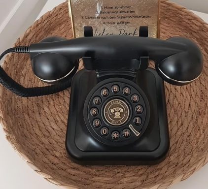 Audiogästebuch Schwarzes Vintage-Telefon mit Wählscheibe auf einem geflochtenen Tisch.