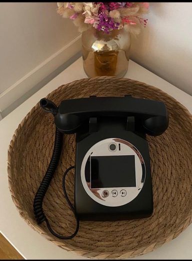 Videogästebuch Schwarzes Telefon auf einem runden Tisch mit einer Vase und Blumen im Hintergrund.